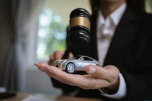 Escritorio de abogado con mazo, contrato y coche de juguete simbolizando justicia, juicio legal, reclamación de seguro y casos de derecho automovilístico.