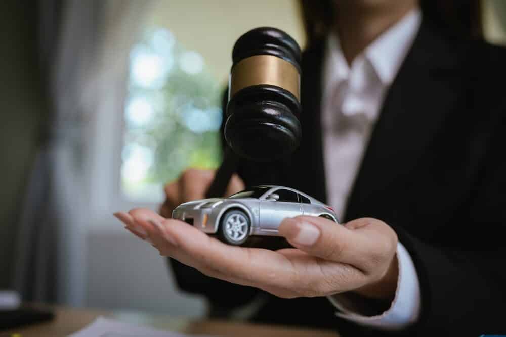 Escritorio de abogado con mazo, contrato y coche de juguete simbolizando justicia, juicio legal, reclamación de seguro y casos de derecho automovilístico.