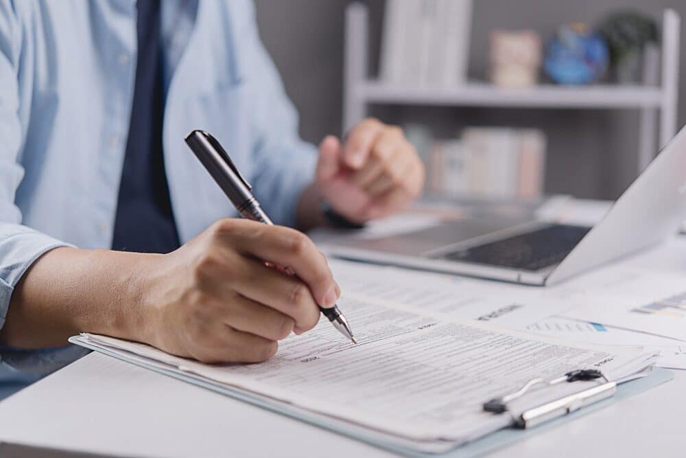 Mano de empresario rellenando un formulario de declaración de impuestos o un documento de solicitud de seguro