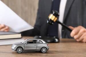 Ley de accidentes de tráfico. Hombre con documento y mazo en mesa de madera en interiores, enfoque en coche de juguete.