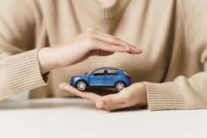 Mano de mujer protegiendo un coche azul, símbolo del seguro de coche y concepto de protección del vehículo.