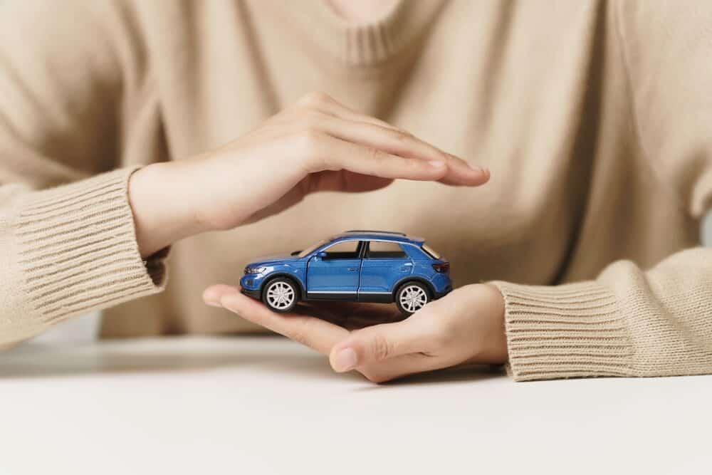 Mano de mujer protegiendo un coche azul, símbolo del seguro de coche y concepto de protección del vehículo.