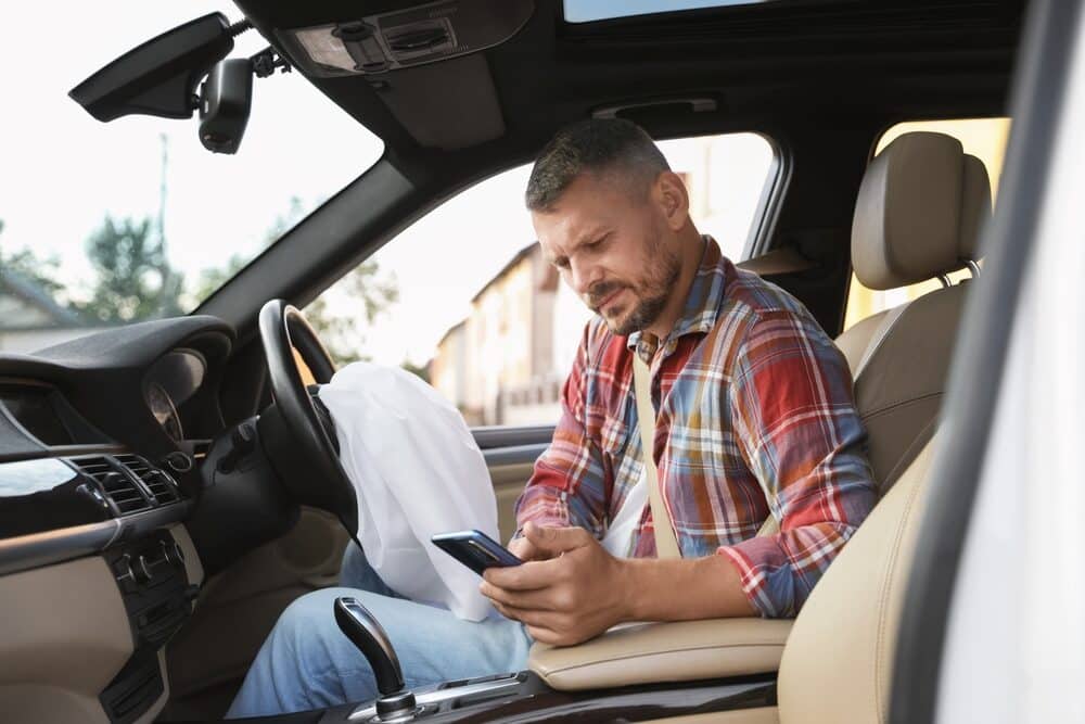 Hombre usando un smartphone cerca de un airbag abierto en un automóvil tras un accidente de coche