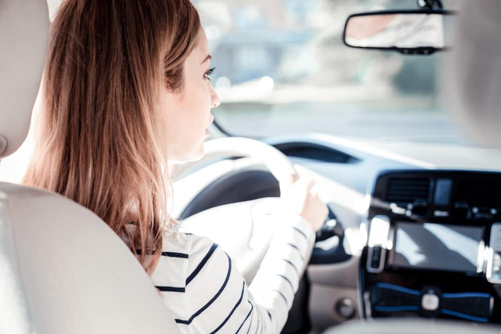 Lo veo todo. Mujer joven cuidadosa y atractiva sentada en su coche sujetando el volante mirando la carretera.