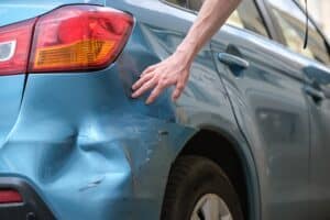 Mano de conductor examinando coche abollado con guardabarros dañado aparcado en la calle de la ciudad. Concepto de seguridad vial y seguro de vehículos.