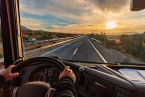 Vista desde el asiento del conductor de un camión de la autopista y un paisaje de campos al amanecer.