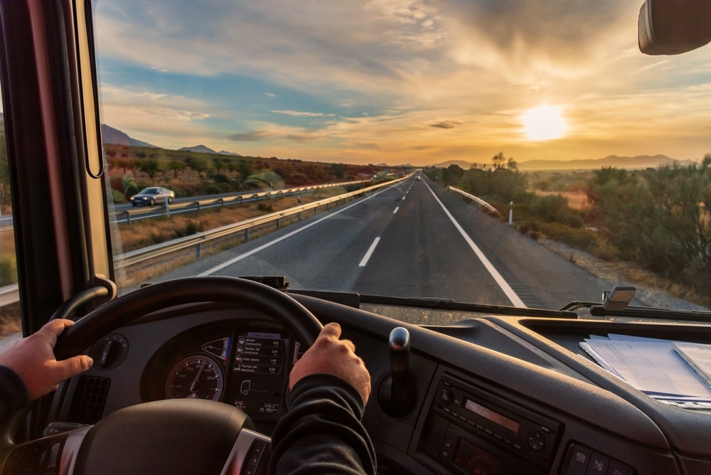 Vista desde el asiento del conductor de un camión de la autopista y un paisaje de campos al amanecer.