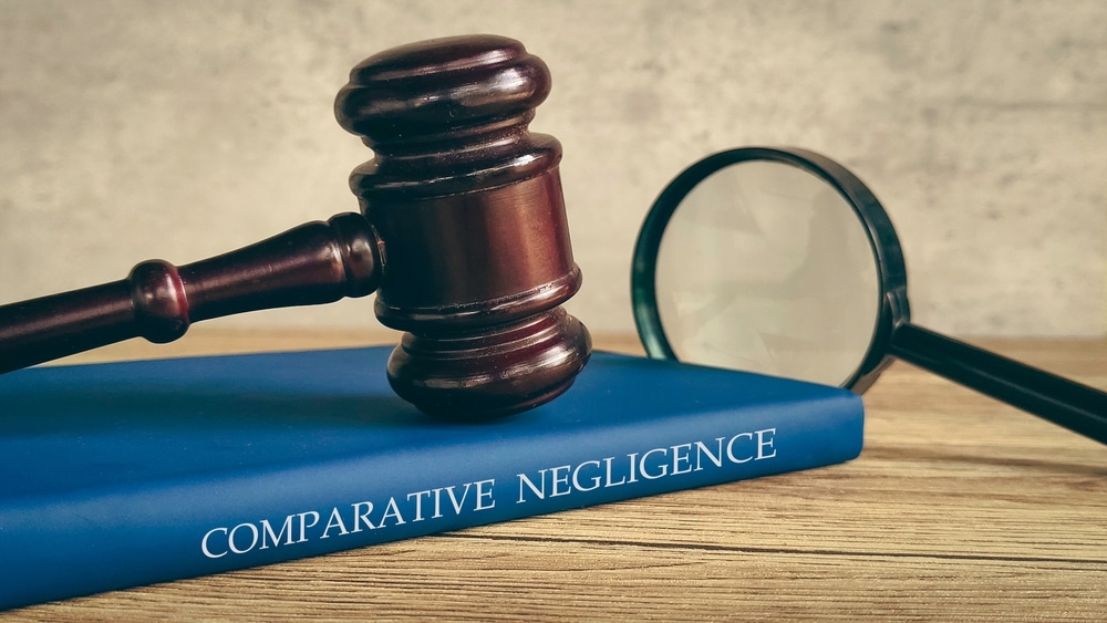 Un mazo y una lupa sobre un libro titulado “NEGLIGENCIA COMPARATIVA”, que simboliza una investigación legal.