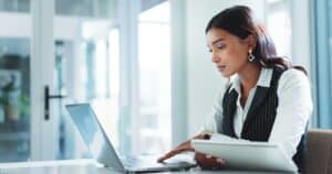 Oficina, mujer seria y de negocios en portátil para seguros, gestión de riesgos o ventas de pólizas en internet.