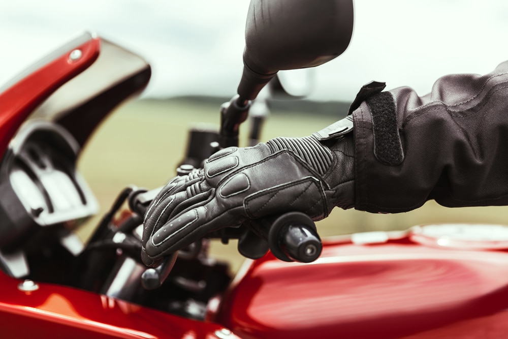 Una mano humana con guantes protectores de moto sujeta una motocicleta y acciona el freno antes de la carrera, primer plano