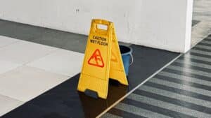 Cartel amarillo con el texto “Precaución, suelo mojado” exhibido en un estacionamiento como forma de cumplir con las leyes de Arizona sobre caídas y resbalones.