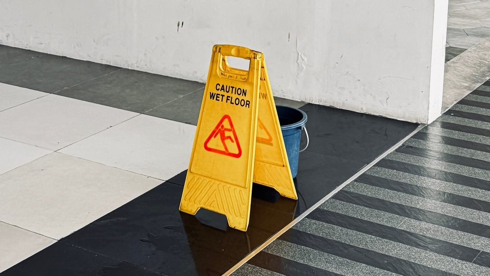 Cartel amarillo con el texto “Precaución, suelo mojado” exhibido en un estacionamiento como forma de cumplir con las leyes de Arizona sobre caídas y resbalones.