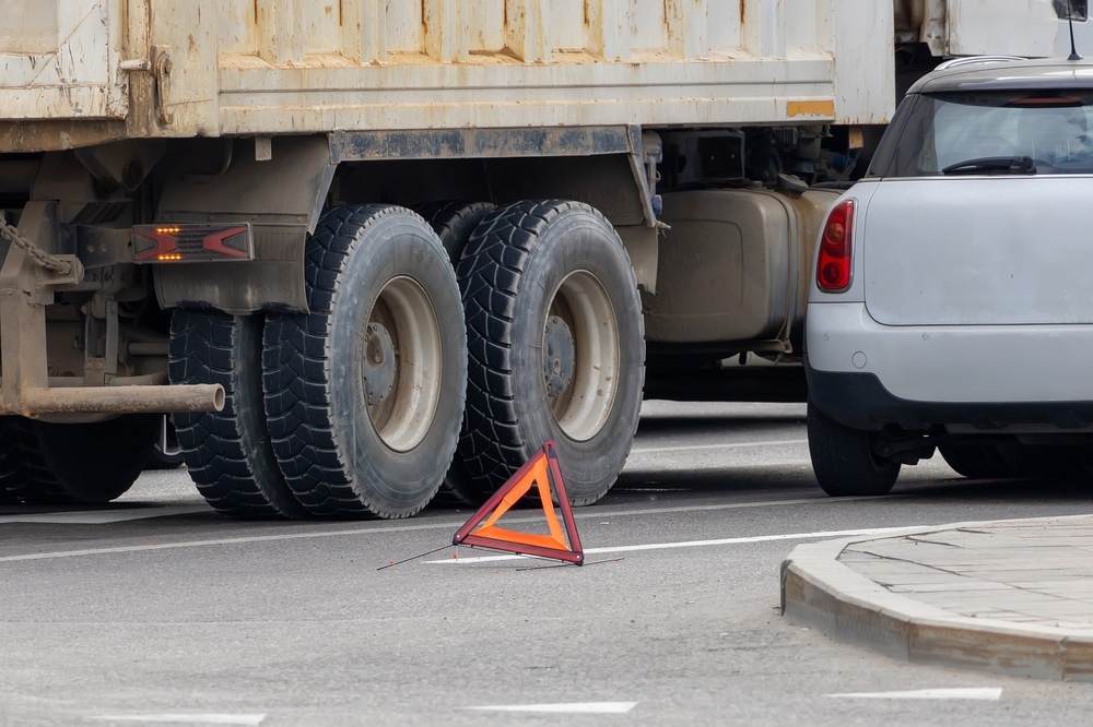 Un camión y un coche chocando en una calle de la ciudad, con un triángulo de advertencia en primer plano. Aprende a evitar accidentes con camiones.